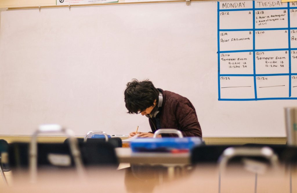 A student writing on paper at a desk in a classroom